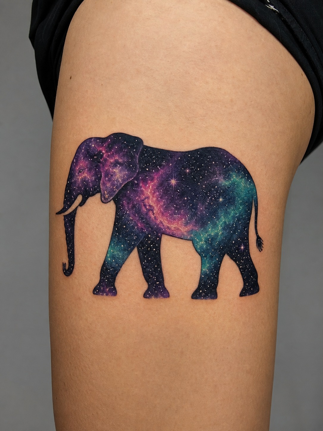 Galaxy elephant tattoo with a cosmic starfield inside a black elephant silhouette.