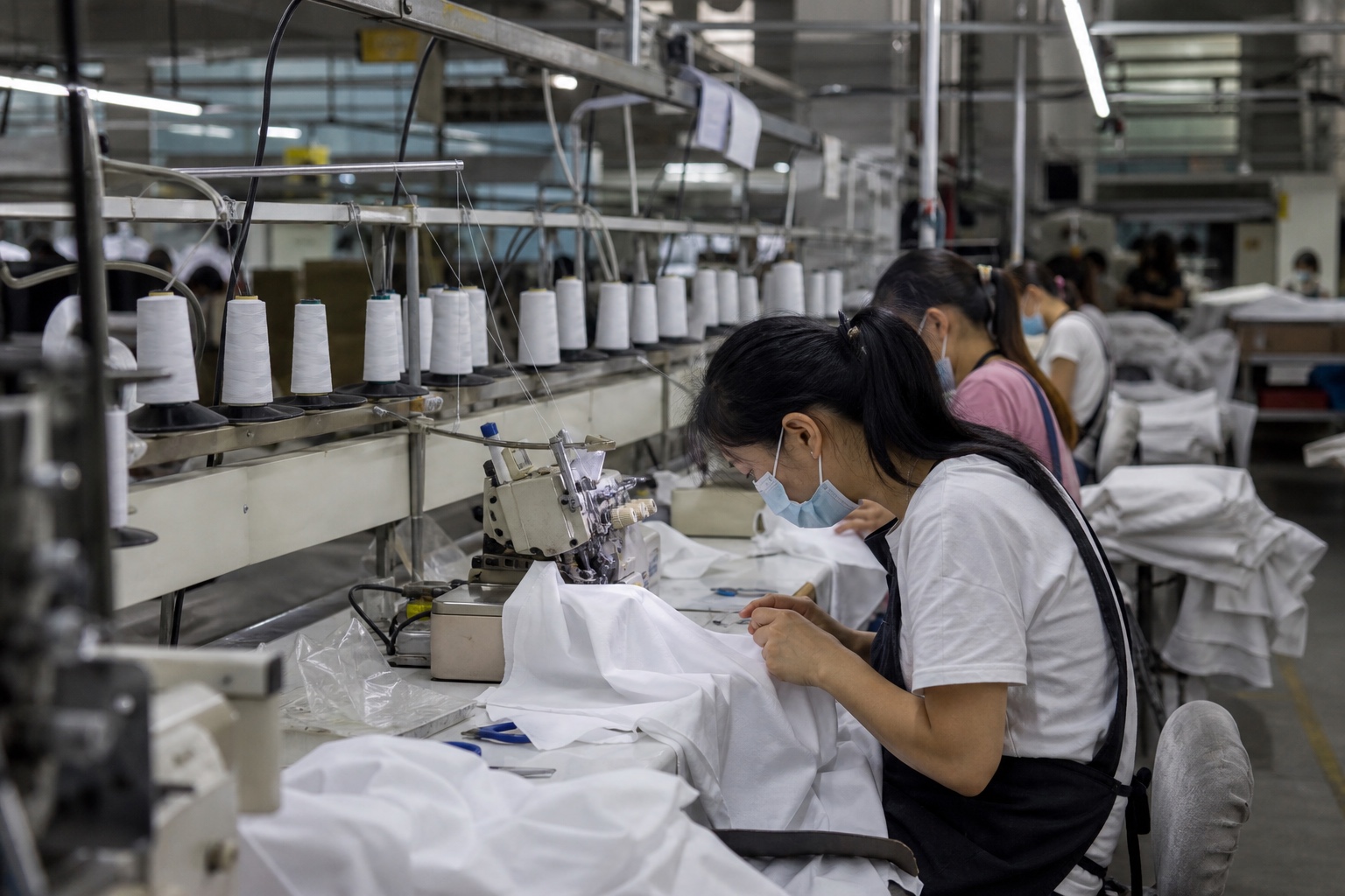 Garment production floor with rows of overlock machines and workers sewing fabric.