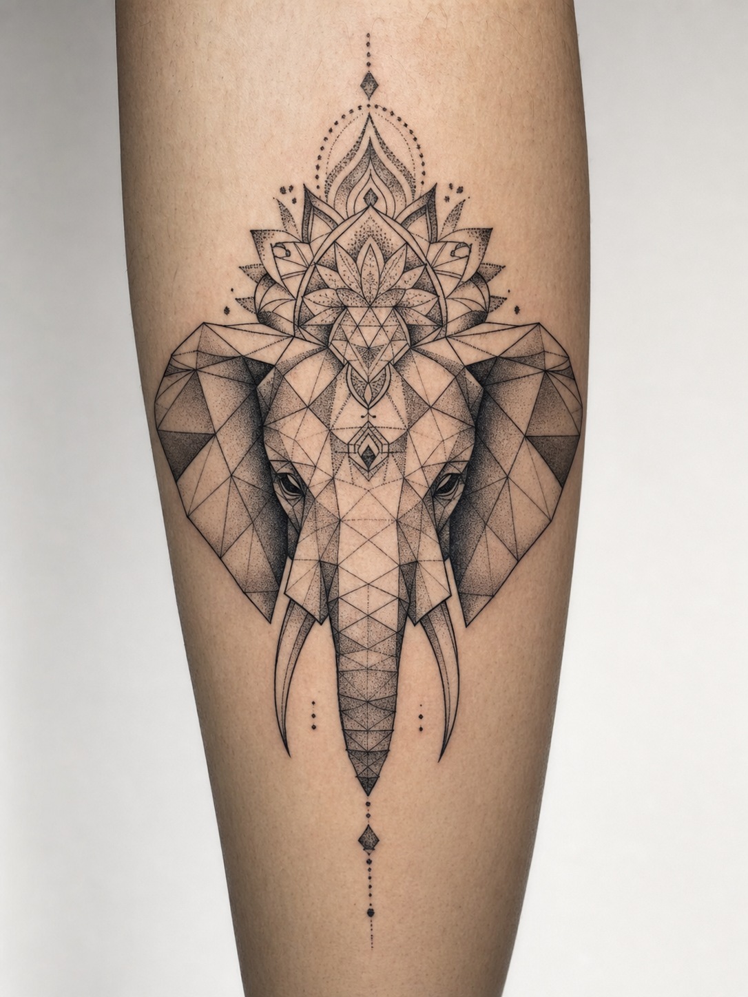 Geometric dotwork elephant head tattoo with triangular facets and mandala details.