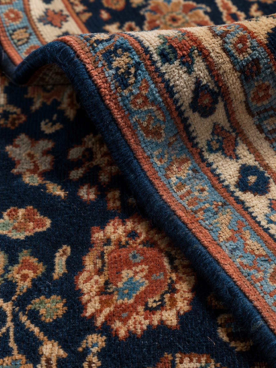 Close-up of a hand-knotted Persian wool carpet with navy and terracotta pattern details.