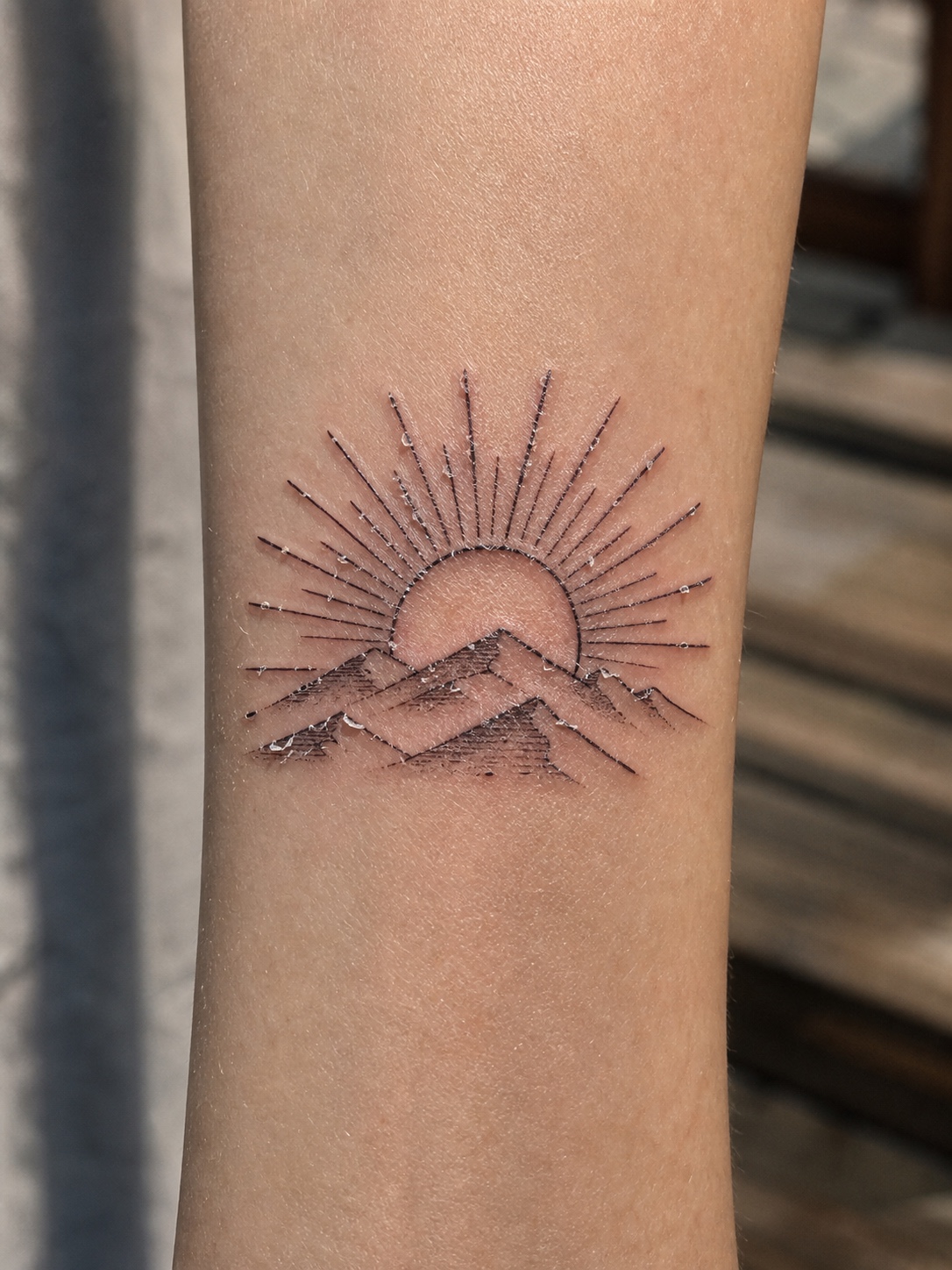 Healing sunrise tattoo on a forearm with light peeling during the first week.