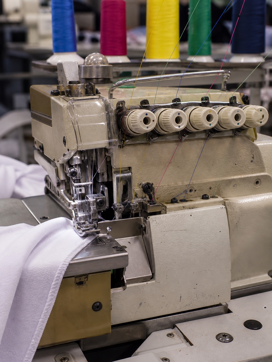 Close view of an industrial overlock machine with thread cones and the needle area in a production studio.