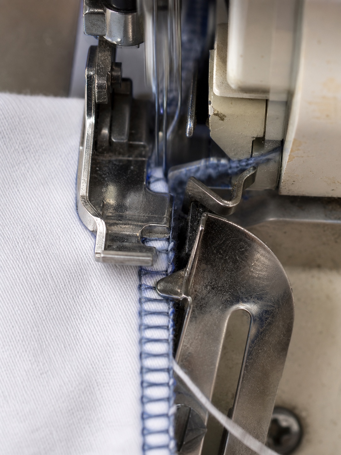 Jersey fabric seam passing under an overlock machine presser foot as the edge is trimmed and stitched.