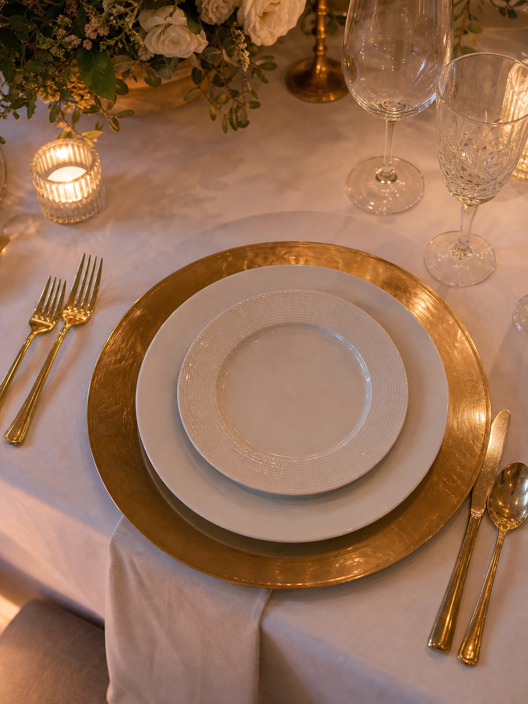 Formal wedding place setting with a gold charger, white dinner plate, and smaller salad plate layered on top.