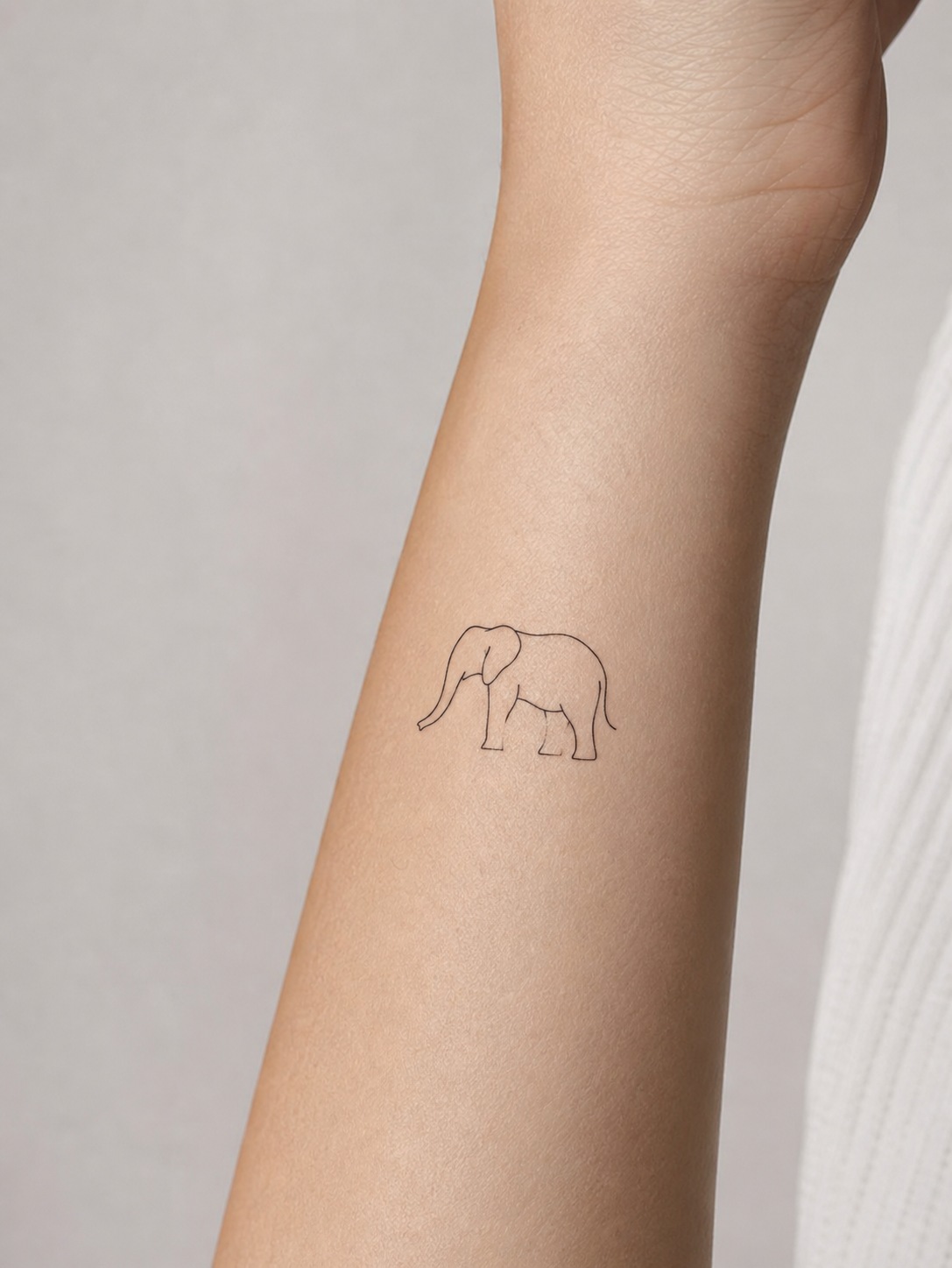 Fine-line elephant outline tattoo sized for a small wrist placement.