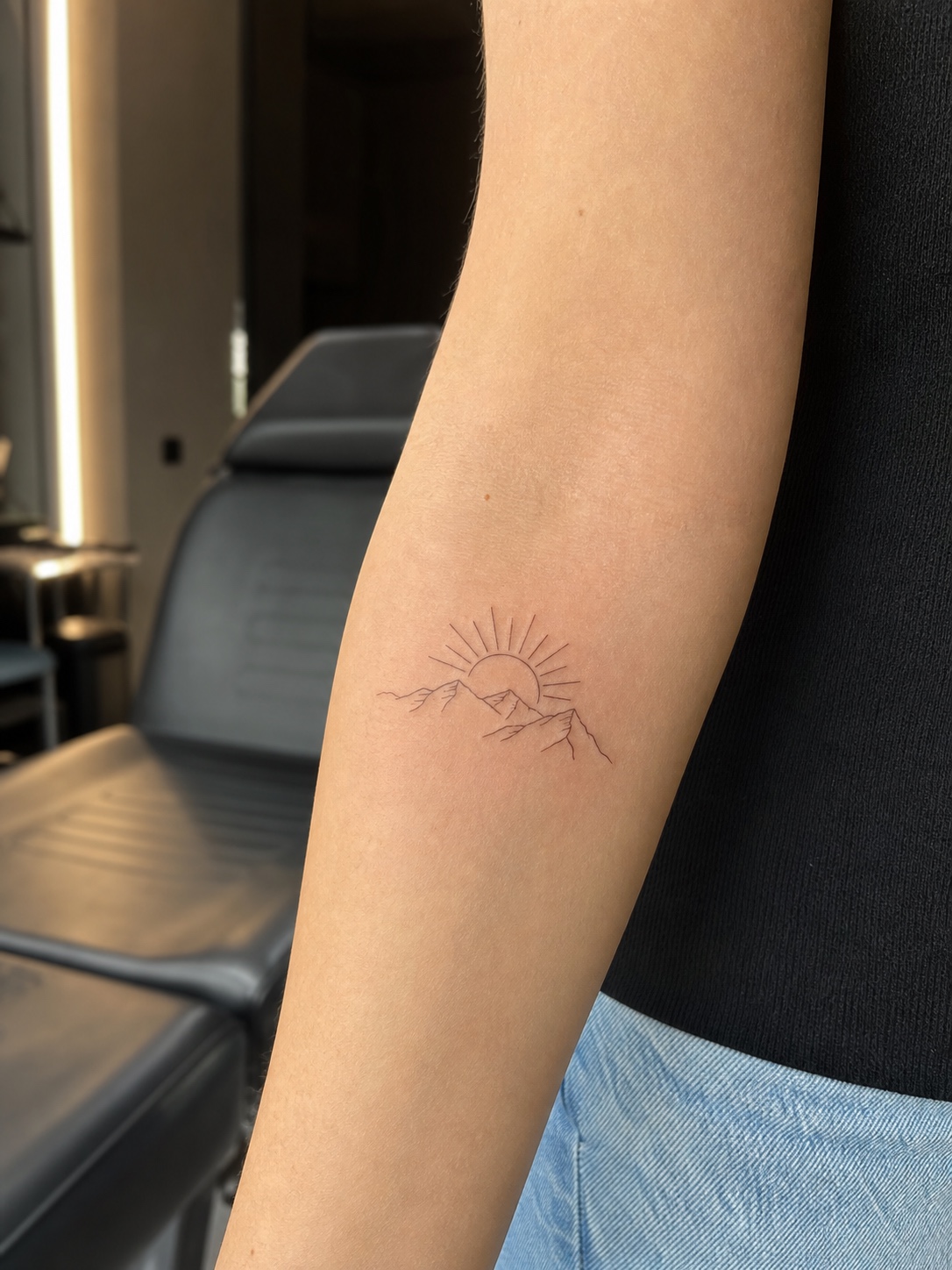 Minimalist fine-line sunrise and mountain tattoo on an inner forearm.