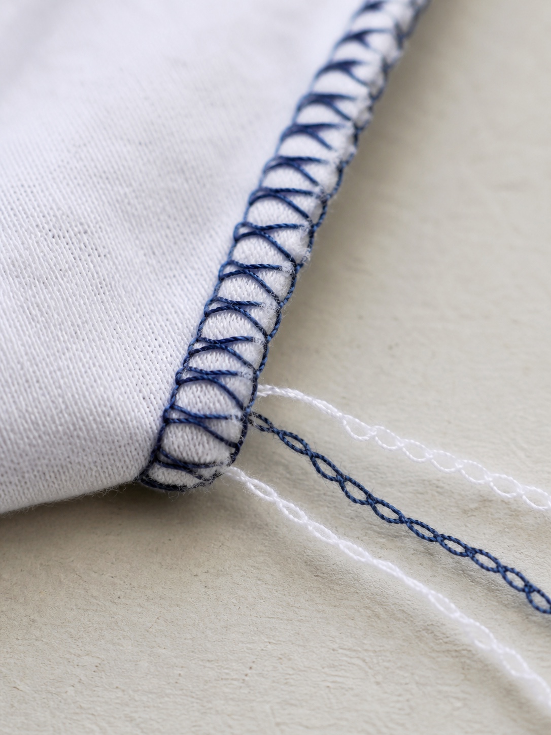 Macro view of looped overlock stitching wrapped around the raw edge of white jersey fabric.