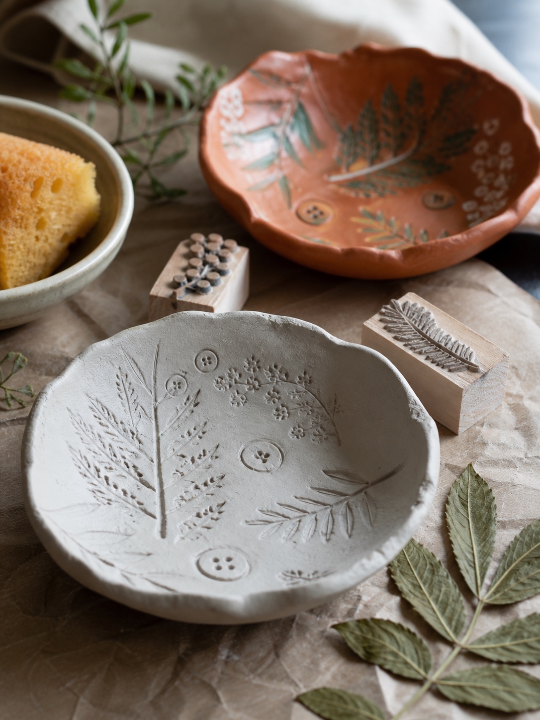 Stamped botanical clay bowl Stamped clay bowl with botanical leaf impressions, wooden stamps, pressed leaves, and a sponge on parchment. | Sky Rye Design Stamped clay bowl with botanical leaf impressions, wooden stamps, pressed leaves, and a sponge on parchment.