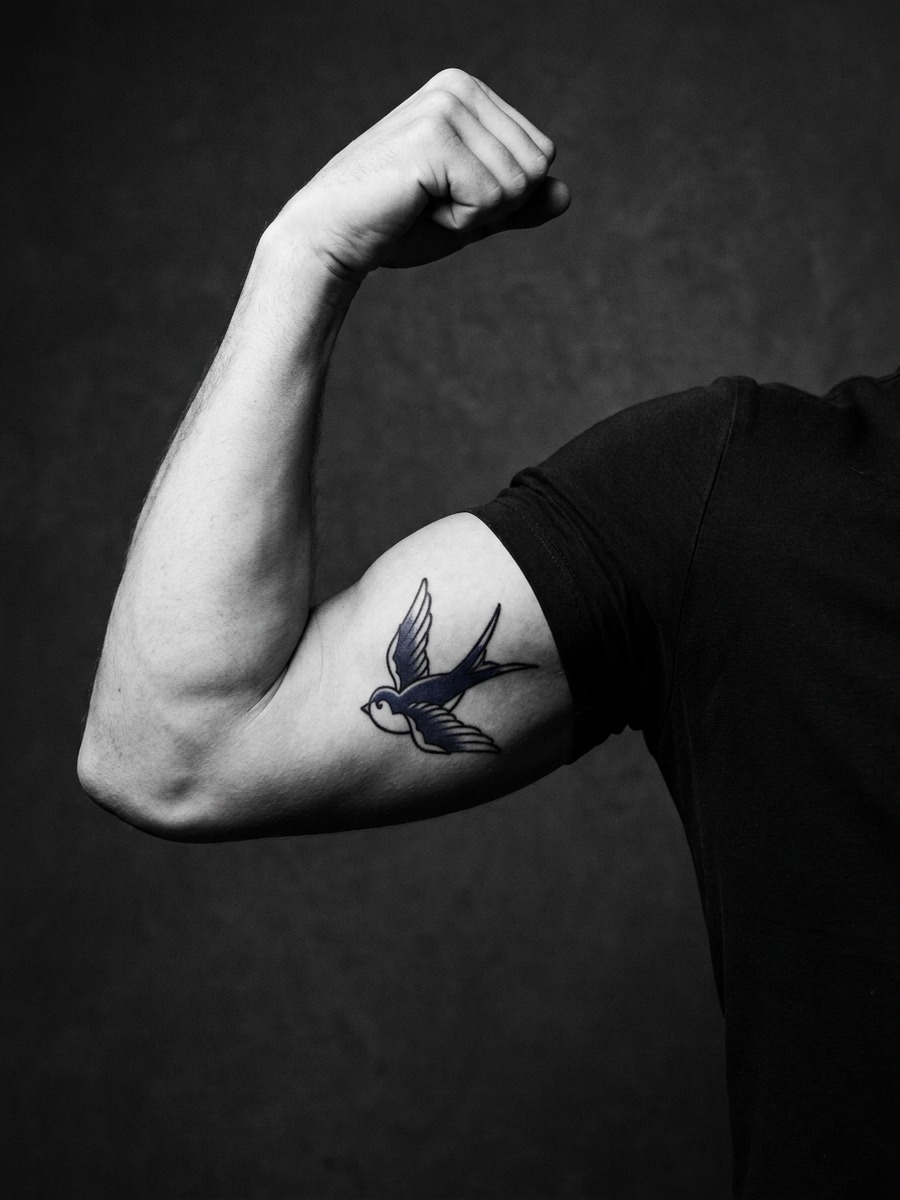 Bold-outline sparrow tattoo perched on a man's bicep and upper arm.