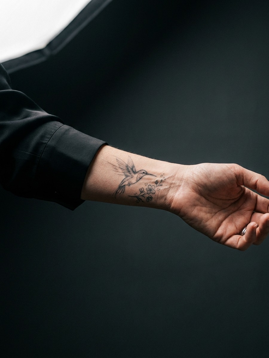 Fine-line hummingbird in mid-hover on a woman's inner wrist.