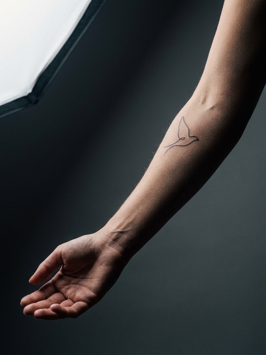 Single continuous-line bird silhouette on a woman's inner forearm.