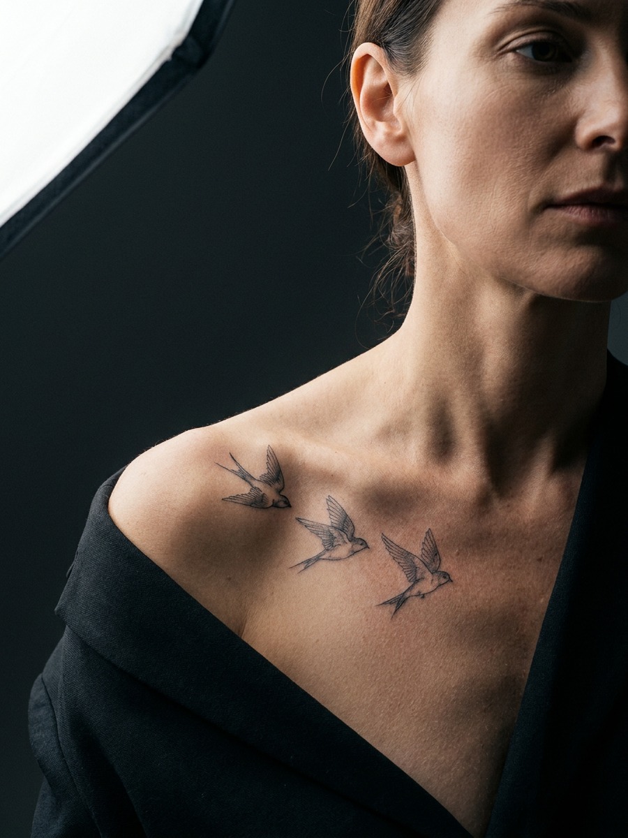 Three fine-line birds in flight on a woman's collarbones and upper chest.