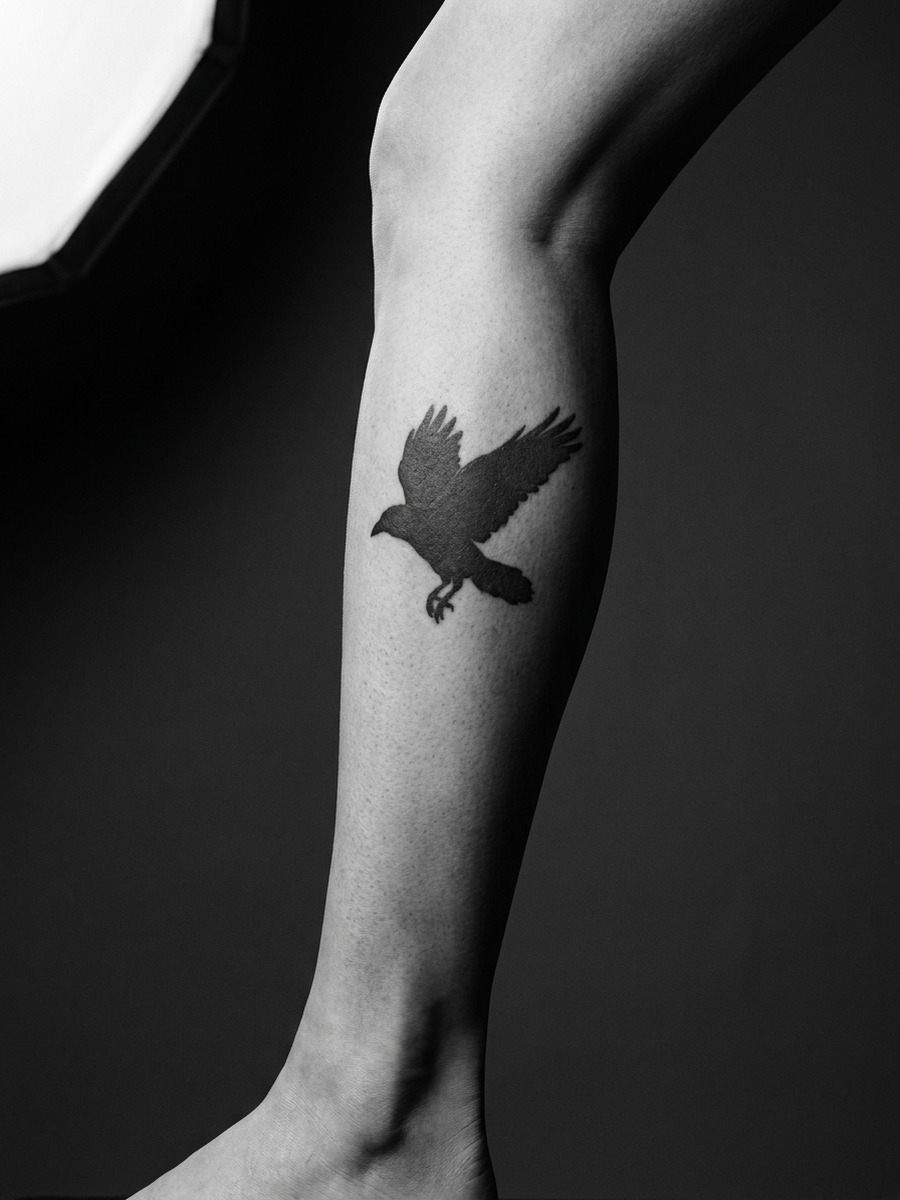 Solid black silhouette raven on a woman's calf.