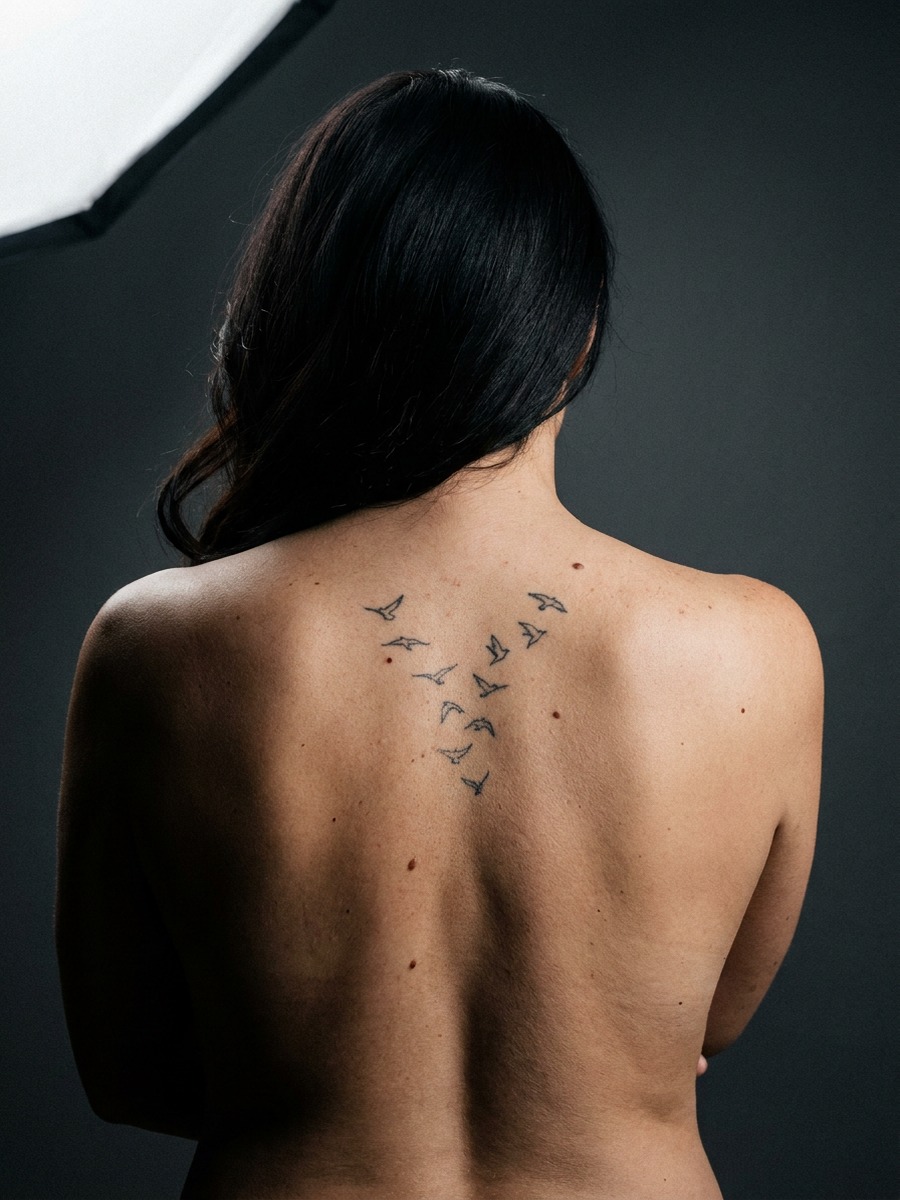 Small birds in a V-formation flock on a woman's upper back and spine.