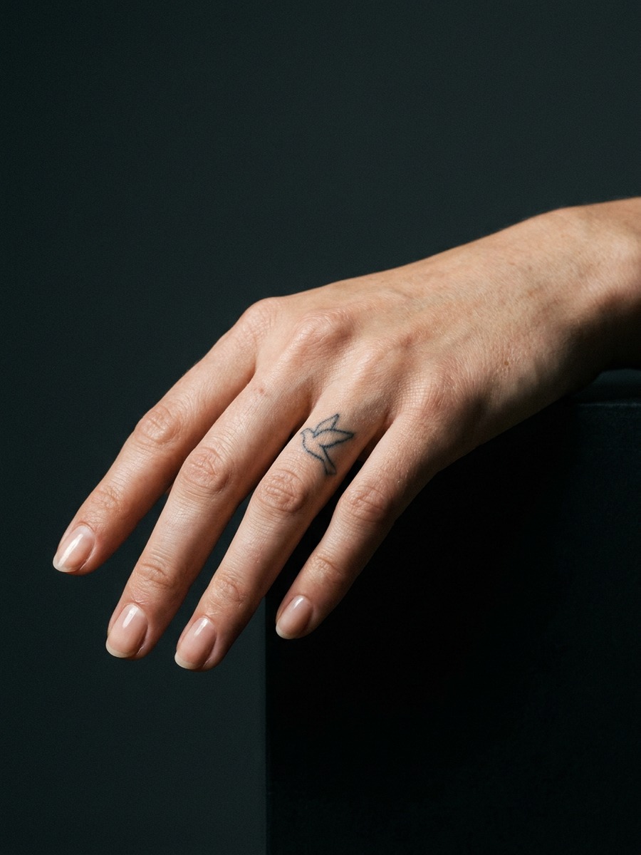 Tiny bird outline on the side of the index finger on a woman's hand.
