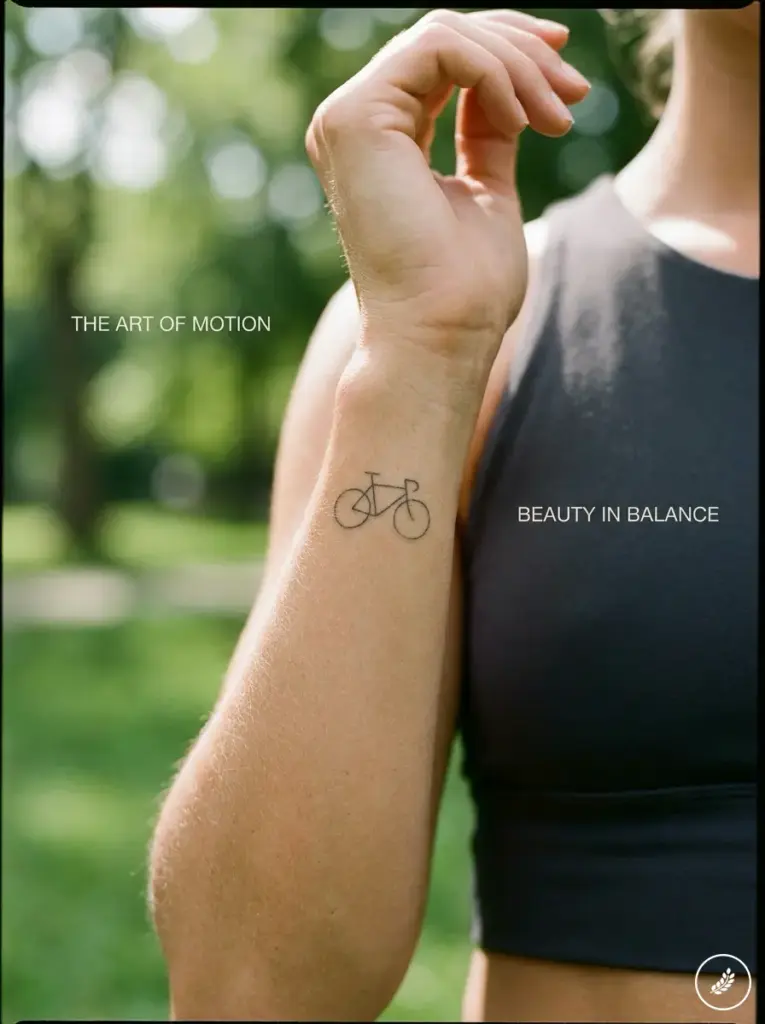 Cyclist_presenting_bicycle_tattoo_202607312349 Close-up of forearm with minimalist bicycle wrist tattoo against a blurred park background and fitness crop top | Sky Rye Design Close-up of forearm with minimalist bicycle wrist tattoo against a blurred park background and fitness crop top