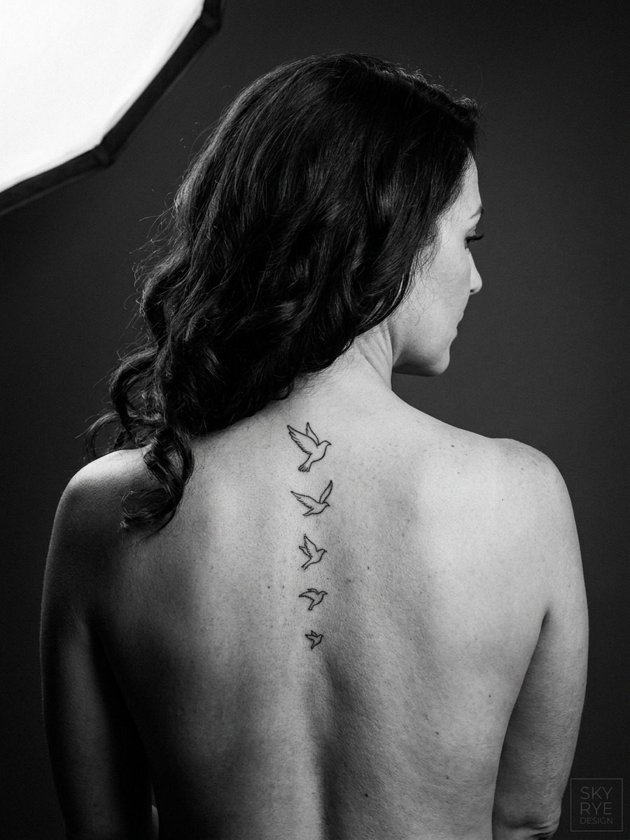 A vertical ladder of five small birds descending the spine on a woman's full back.