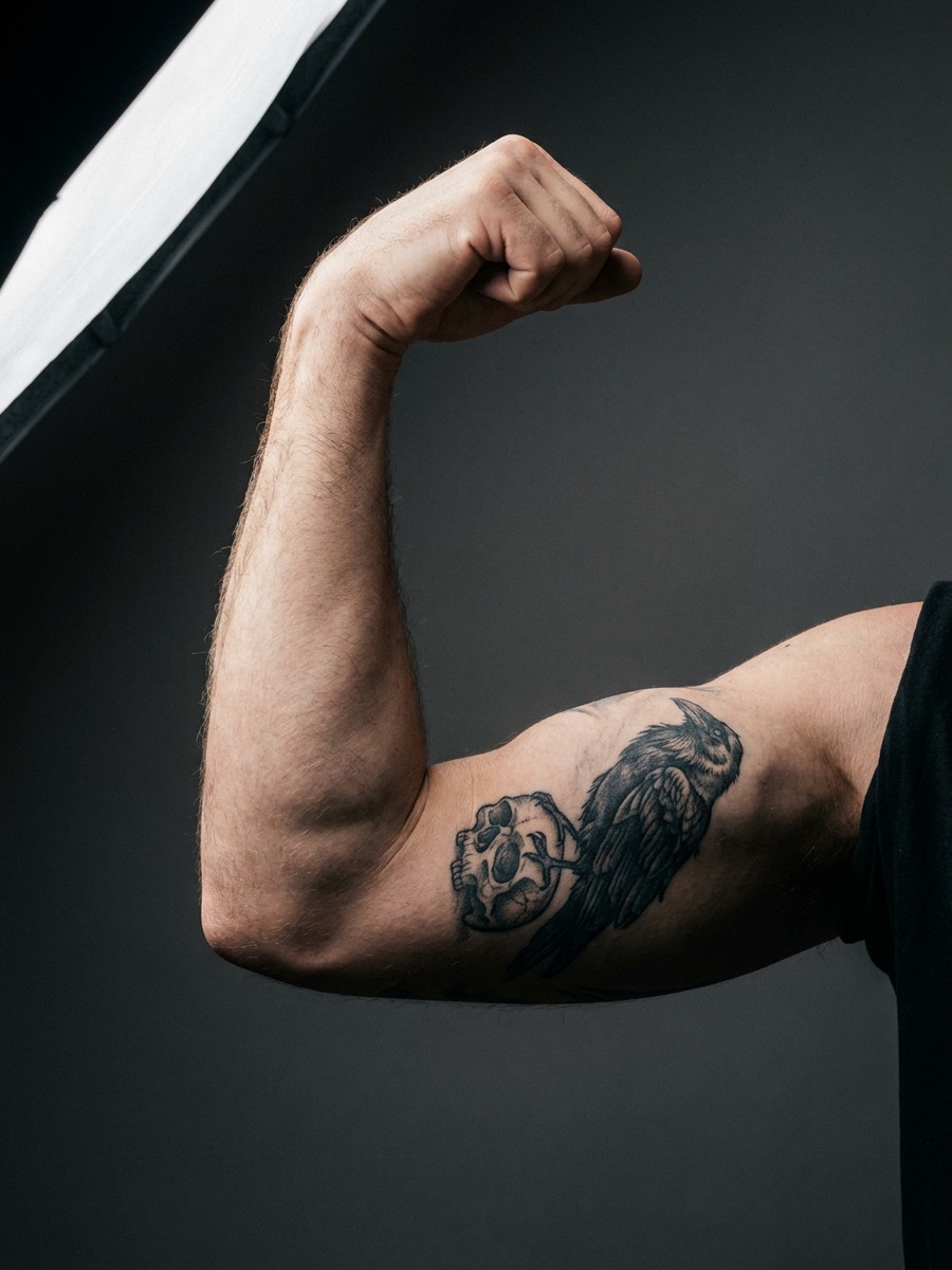 A raven perched atop a small skull on a man's forearm.