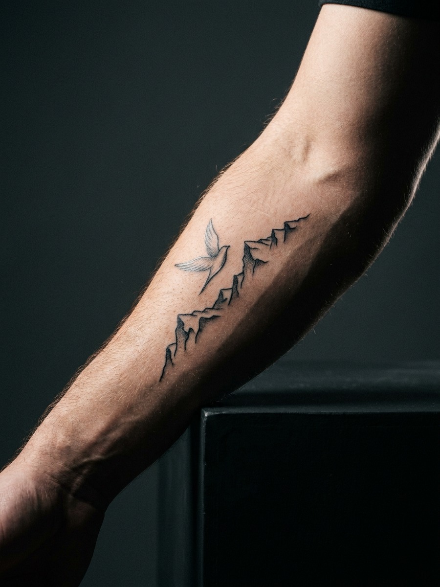 A bird in flight above a jagged mountain range silhouette on a man's forearm.