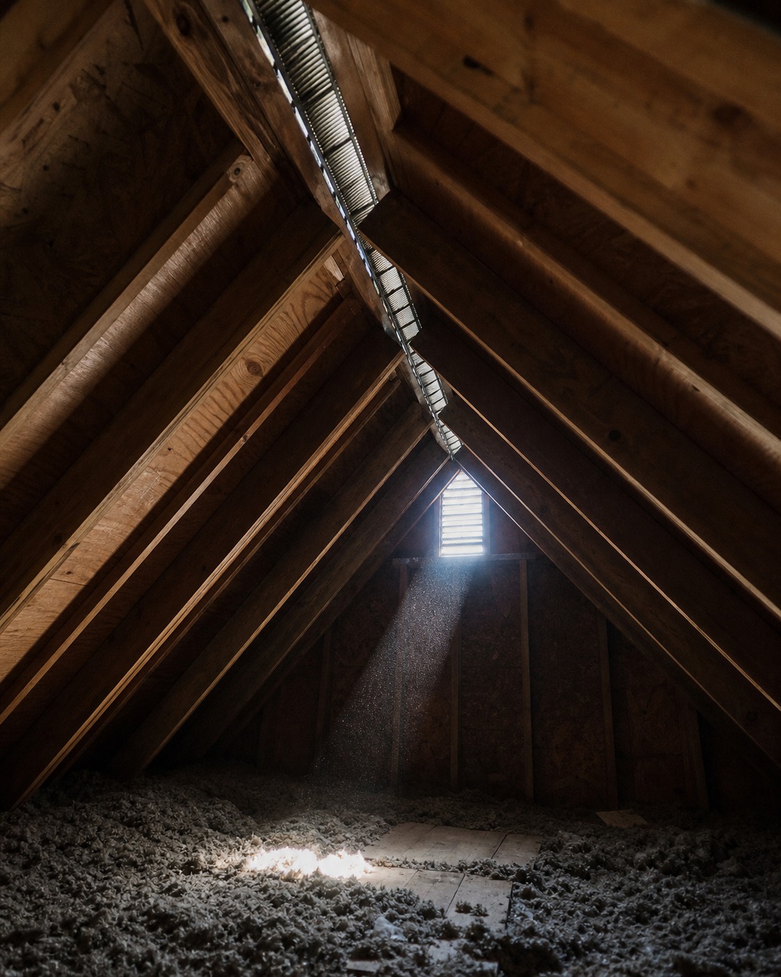 Dim attic interior with rafters, ridge vent, insulation, and a shaft of daylight