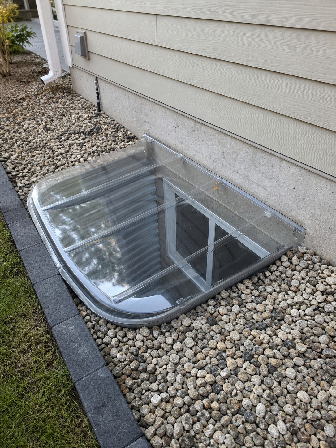 Window Well With Cover Below-grade basement window well with gravel, clean edging, and a clear protective cover. | Sky Rye Design Below-grade basement window well with gravel, clean edging, and a clear protective cover.