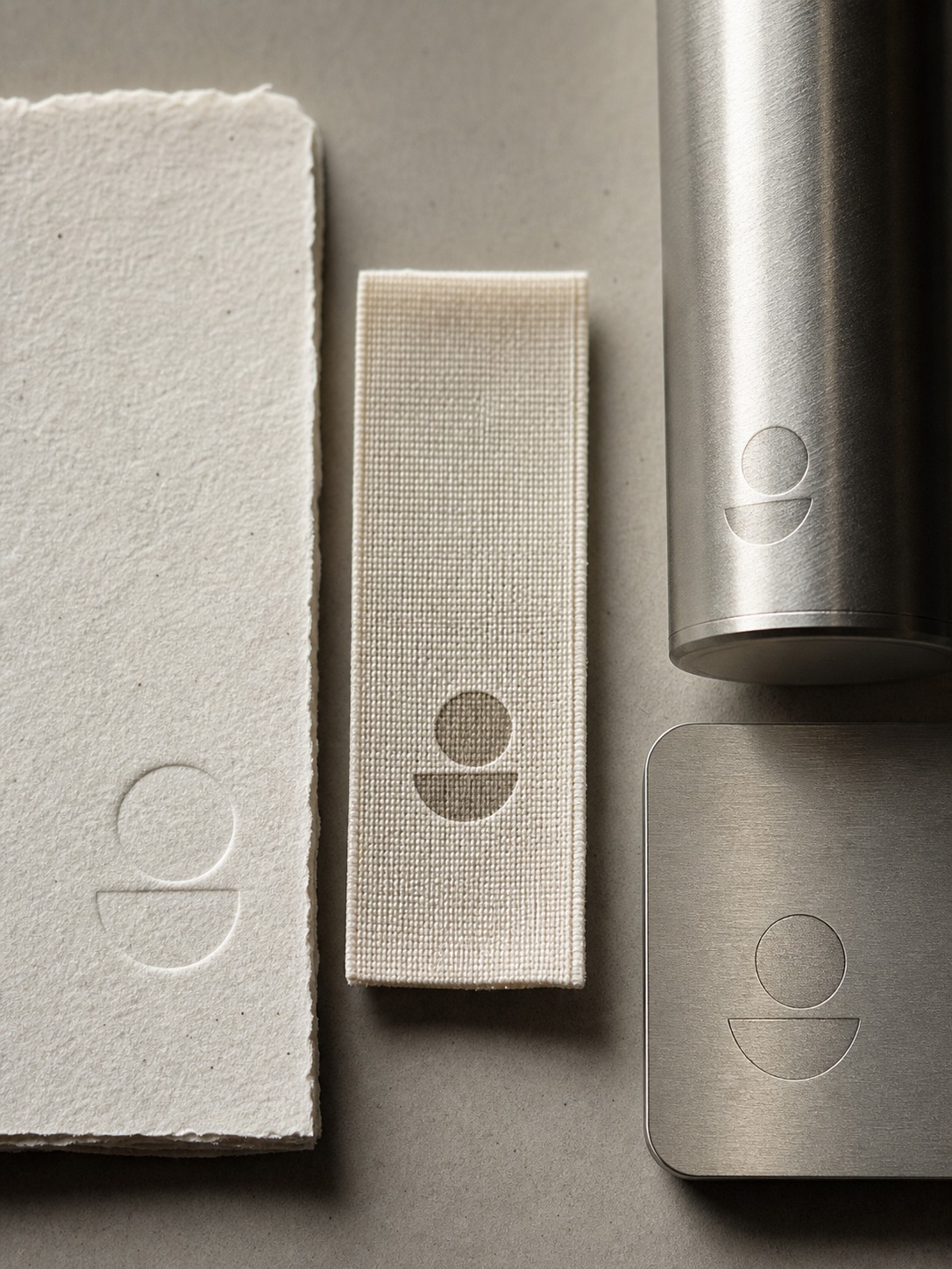 Brand material comparison Textured paper, woven fabric, and brushed metal branded materials arranged side by side. | Sky Rye Design Textured paper, woven fabric, and brushed metal branded materials arranged side by side.