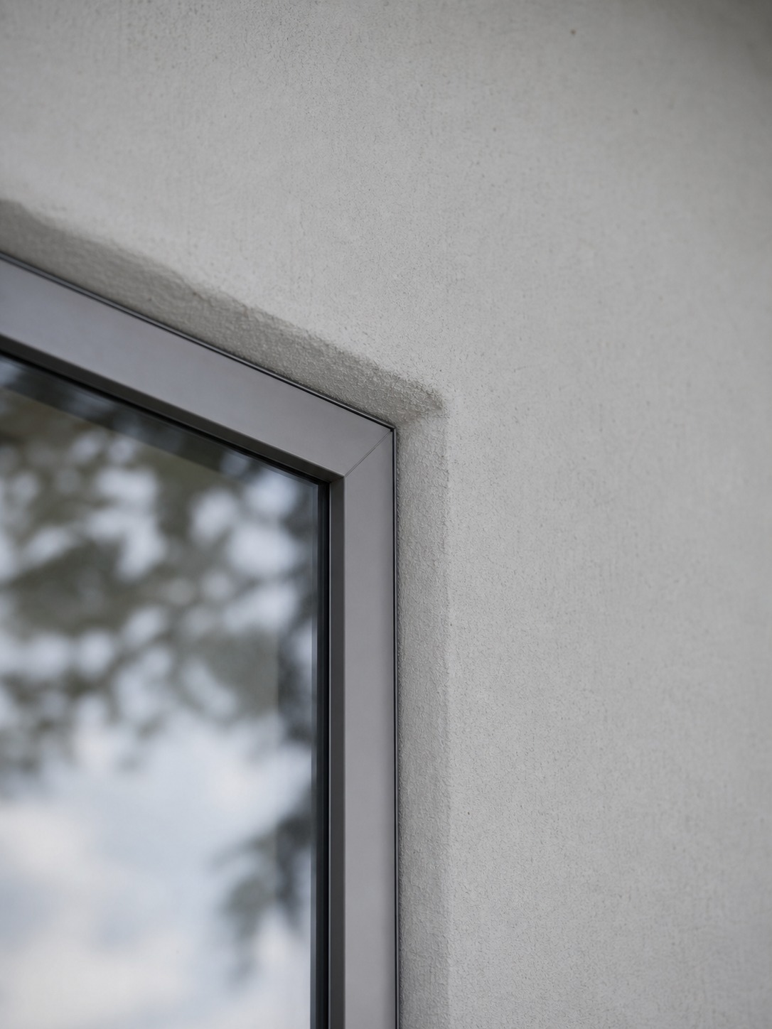 Close detail of a casement window frame meeting a plaster wall with a crisp thin sightline and precise reveal.