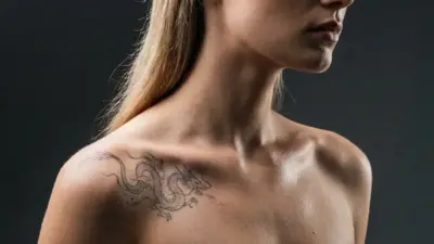 Side-profile studio portrait of a blonde woman in a black strapless top, showcasing a dragon shoulder tattoo