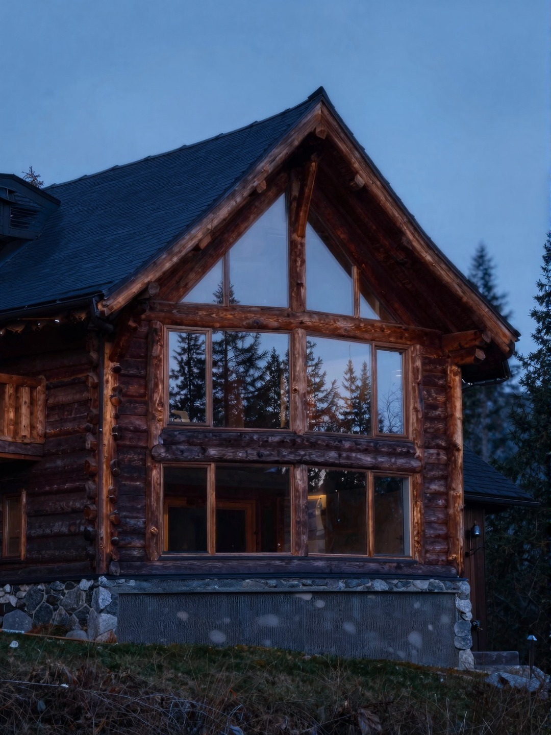 Mountain timber dream house exterior with exposed beams, stone base, dark roof, and forest reflections.