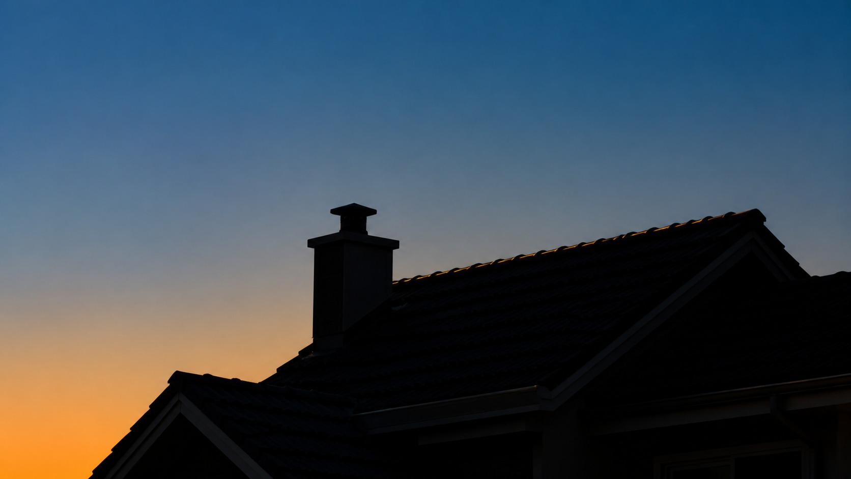 Finished roofline and chimney silhouetted against a blue and amber dusk sky