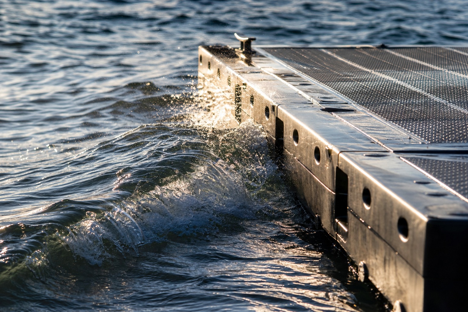 Floating platform edge riding a small wave with spray catching late sunlight.