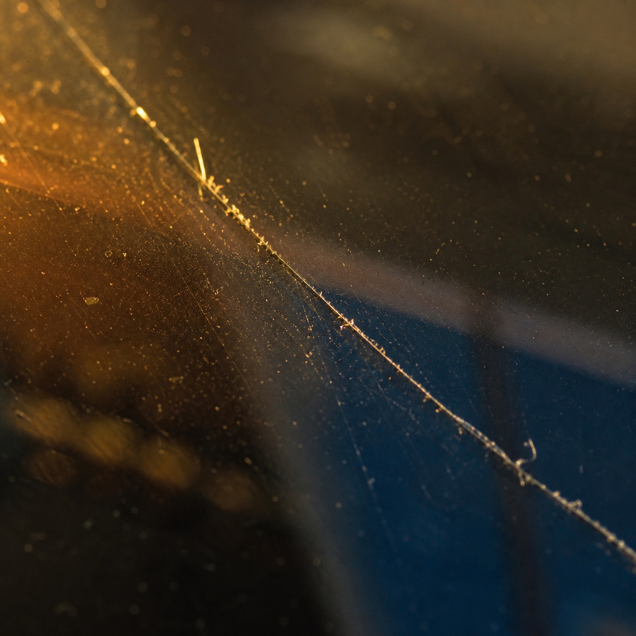 Hairline crack in raking evening light Close macro view of a hairline crack in window glass catching warm raking light. | Sky Rye Design Close macro view of a hairline crack in window glass catching warm raking light.