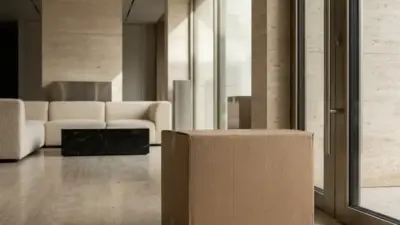 Cardboard moving box on marble floor in modern minimalist living room with beige sofa and floor-to-ceiling windows.