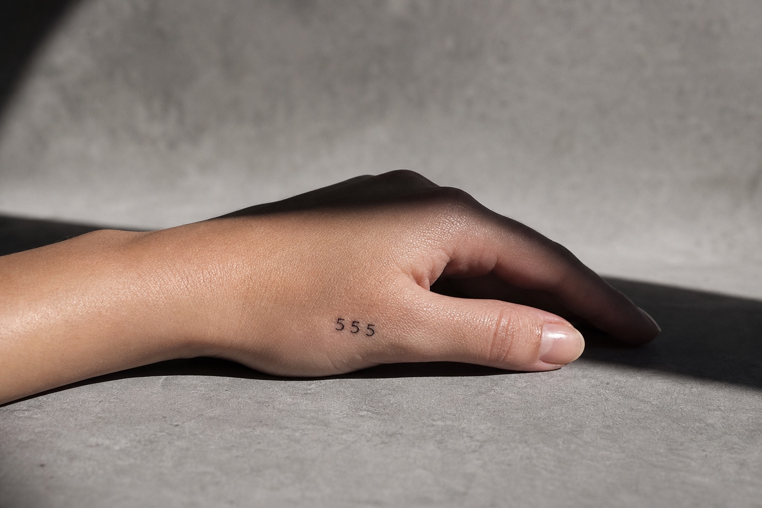 Minimal feminine back of hand tattoo with the angel number 555 in fine black ink