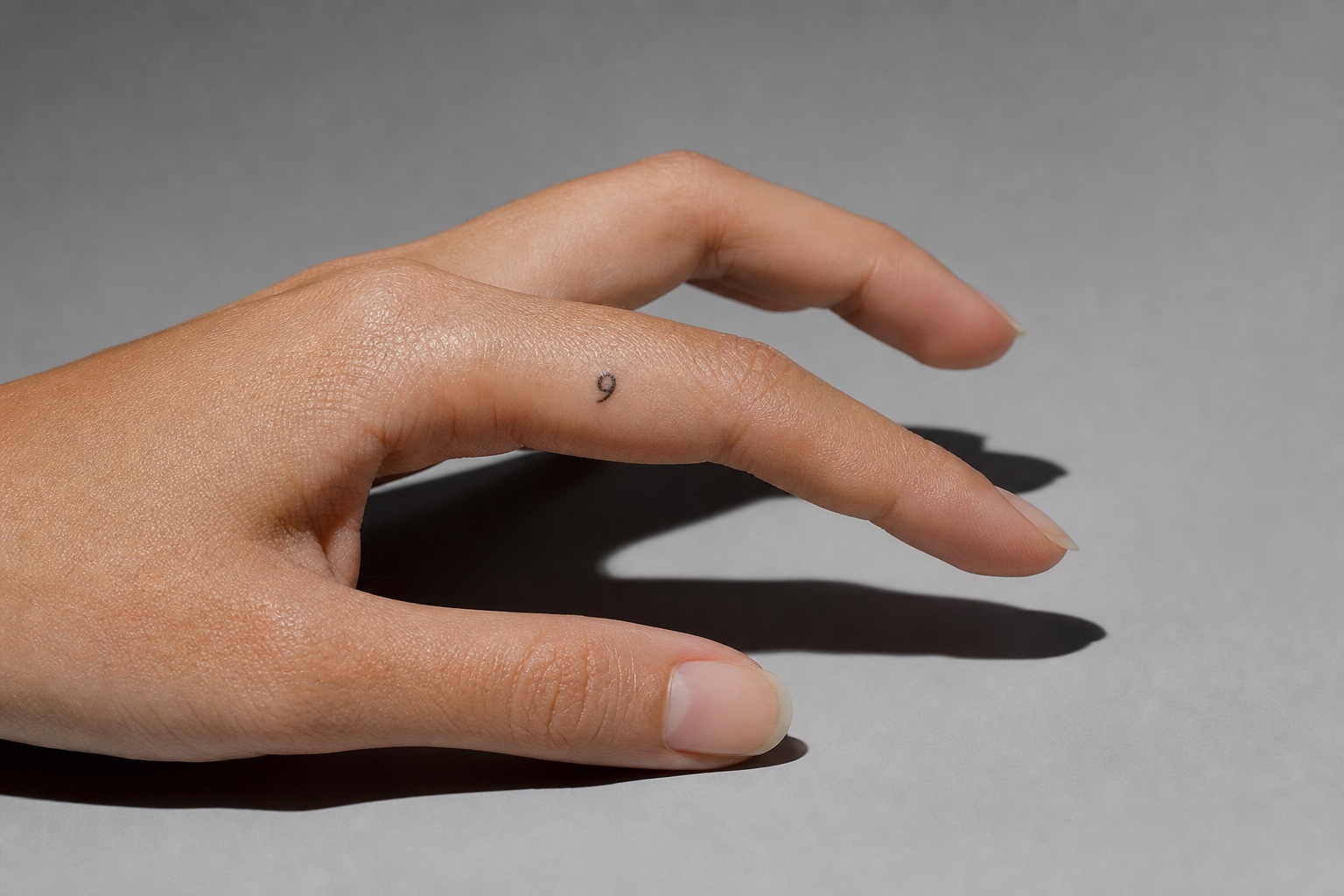 Minimal feminine finger tattoo with a tiny number 9 in fine black ink