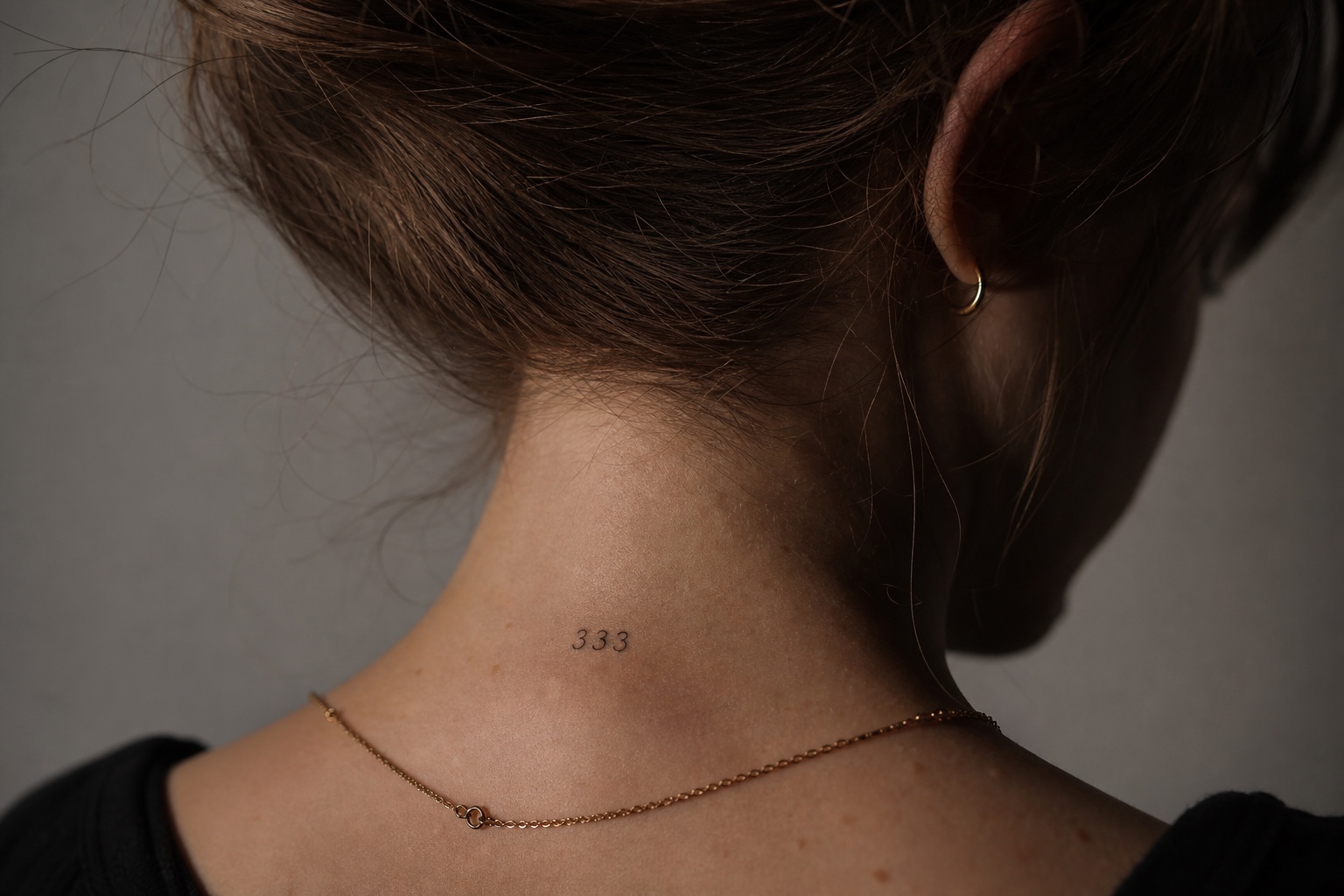Minimal feminine nape tattoo with the angel number 333 in fine black ink
