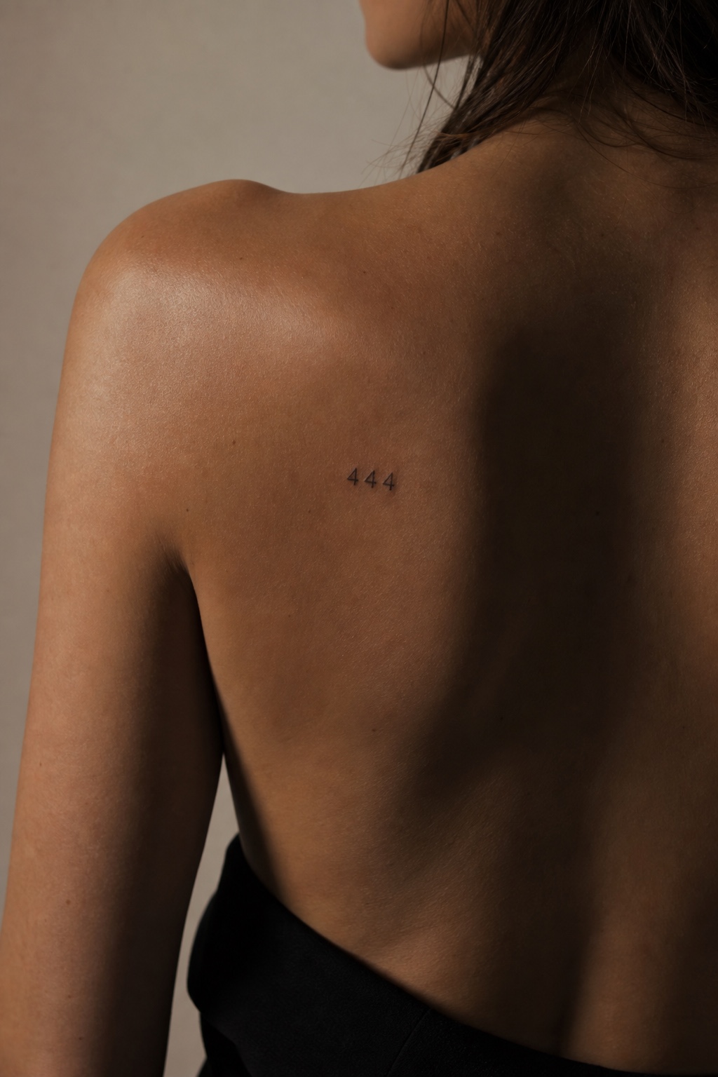 Minimal feminine shoulder blade tattoo with the lucky number 444 in fine black ink