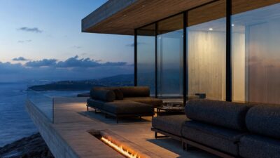 Minimalist outdoor living room on a cantilevered concrete deck with charcoal seating and a linear fire feature at blue hour