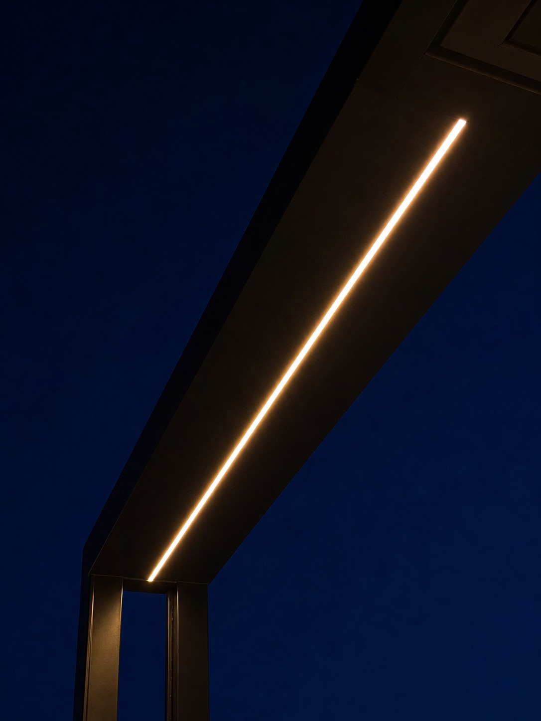 Linear pergola lighting for an outdoor room Upward view of a minimalist steel pergola with a warm recessed linear LED against an indigo sky | Sky Rye Design Upward view of a minimalist steel pergola with a warm recessed linear LED against an indigo sky