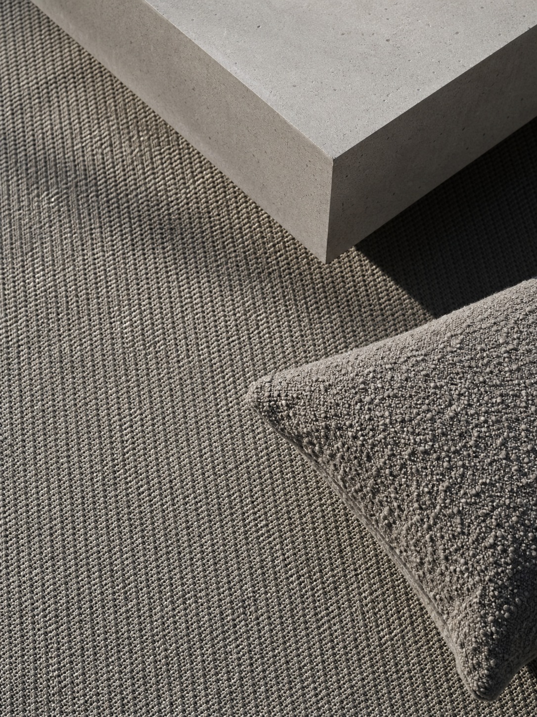 Outdoor rug and boucle cushion texture detail Close flat-lay of a minimalist outdoor rug, concrete coffee table, and boucle cushion in hard daylight | Sky Rye Design Close flat-lay of a minimalist outdoor rug, concrete coffee table, and boucle cushion in hard daylight