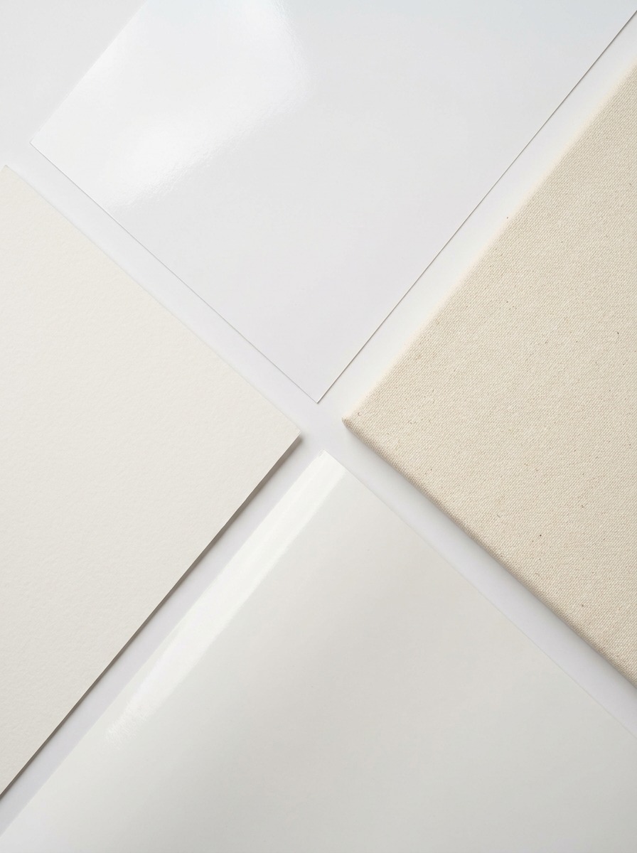 Poster substrate samples Abstract composition of white and off-white papers and a beige fabric swatch arranged in a geometric layout. | Sky Rye Design Gloss, matte, canvas, and vinyl poster substrates arranged for comparison.