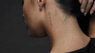 Serenity word tattoo behind the ear and along the nape in delicate script lettering.