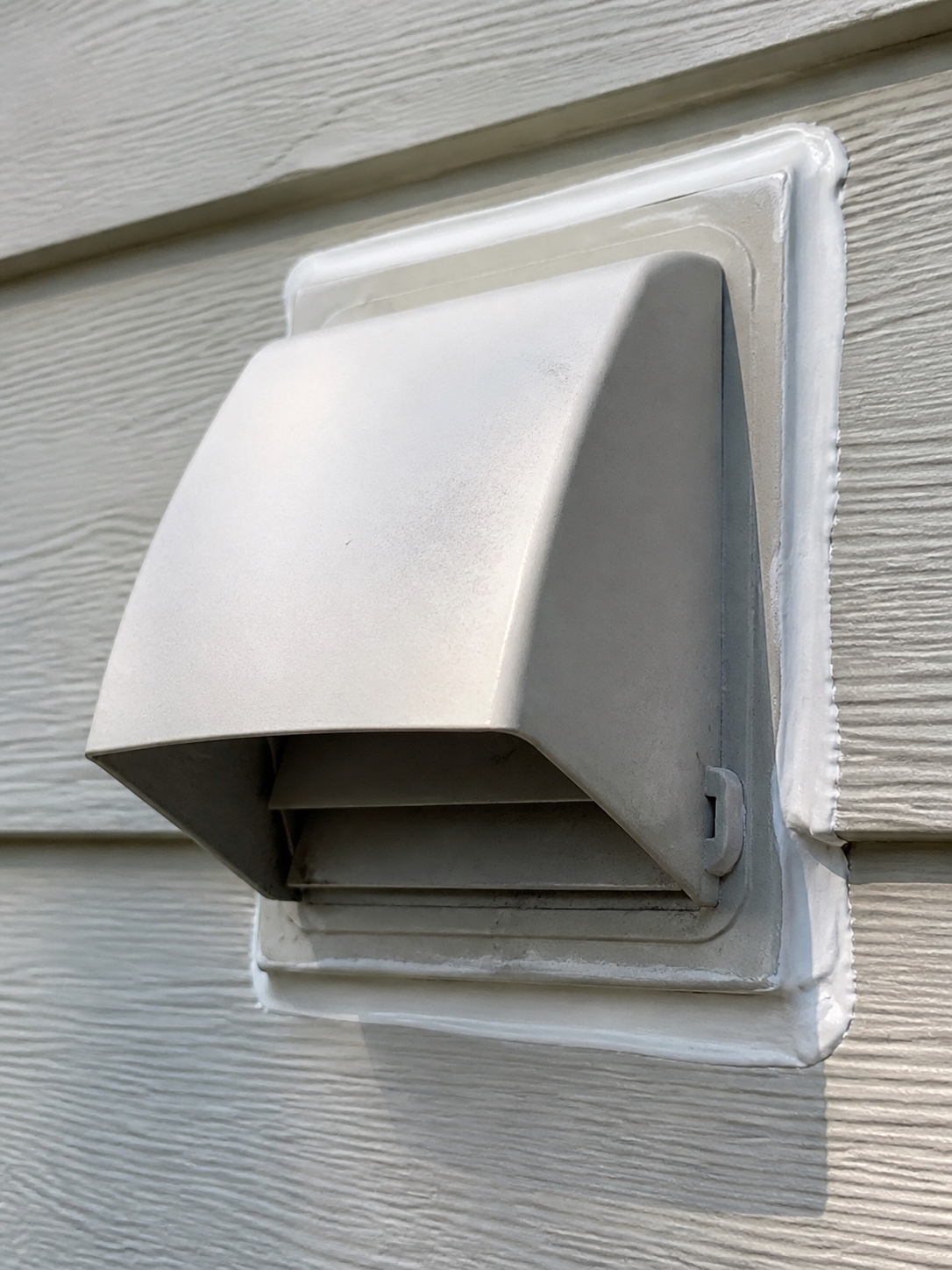 Close-up of a properly sealed dryer vent hood with a clean caulk line against siding.