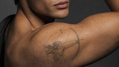 A fine-line Sagittarius archer tattoo with geometric dotwork on a male model’s shoulder.