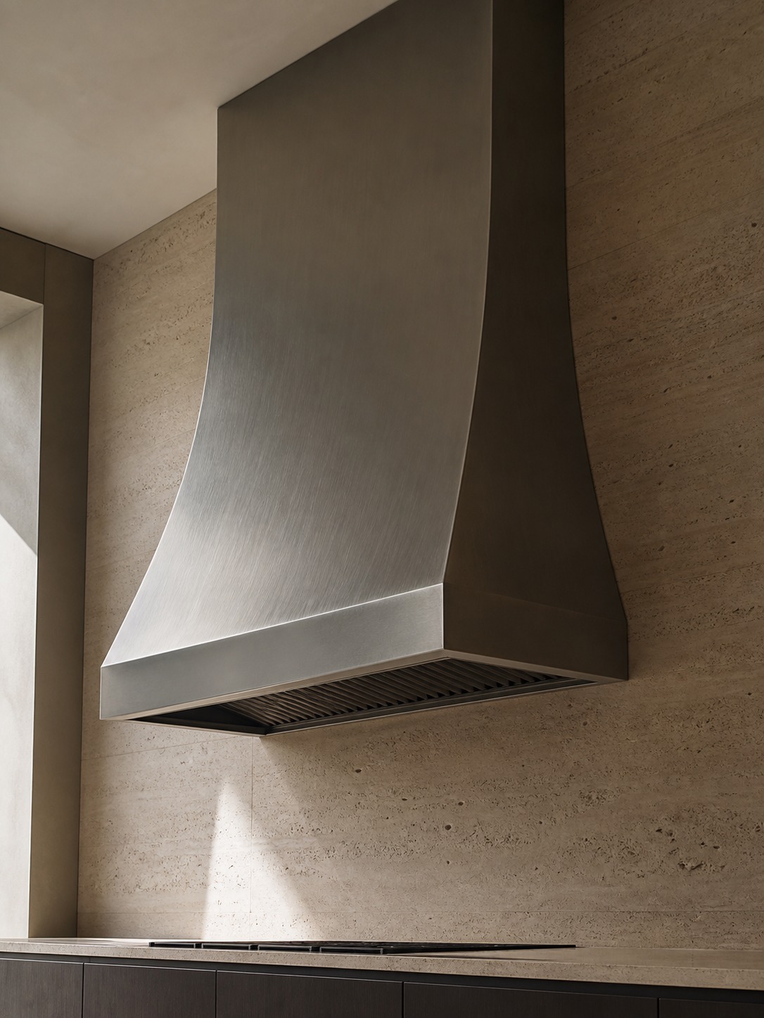 Sculptural brushed metal range hood on stone wall Sculptural brushed metal range hood centered above a stone-clad cooking wall. | Sky Rye Design Sculptural brushed metal range hood centered above a stone-clad cooking wall.