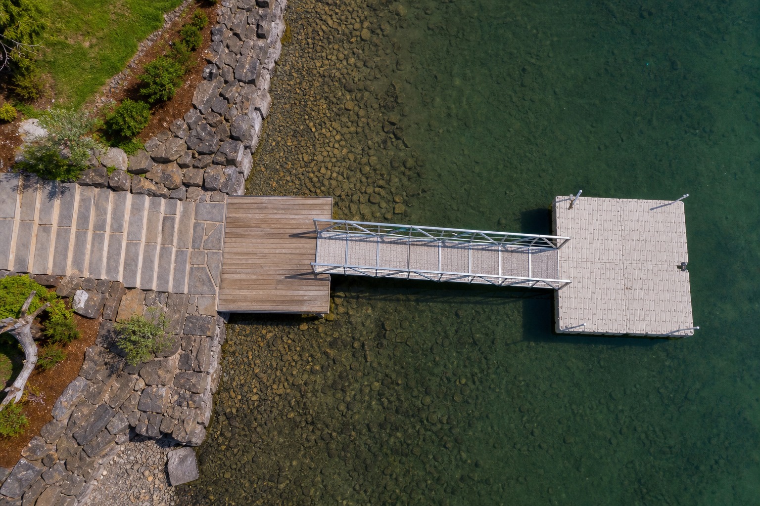 Overhead aerial view of stone steps, a landing, a gangway, and a floating platform aligned from land to water.