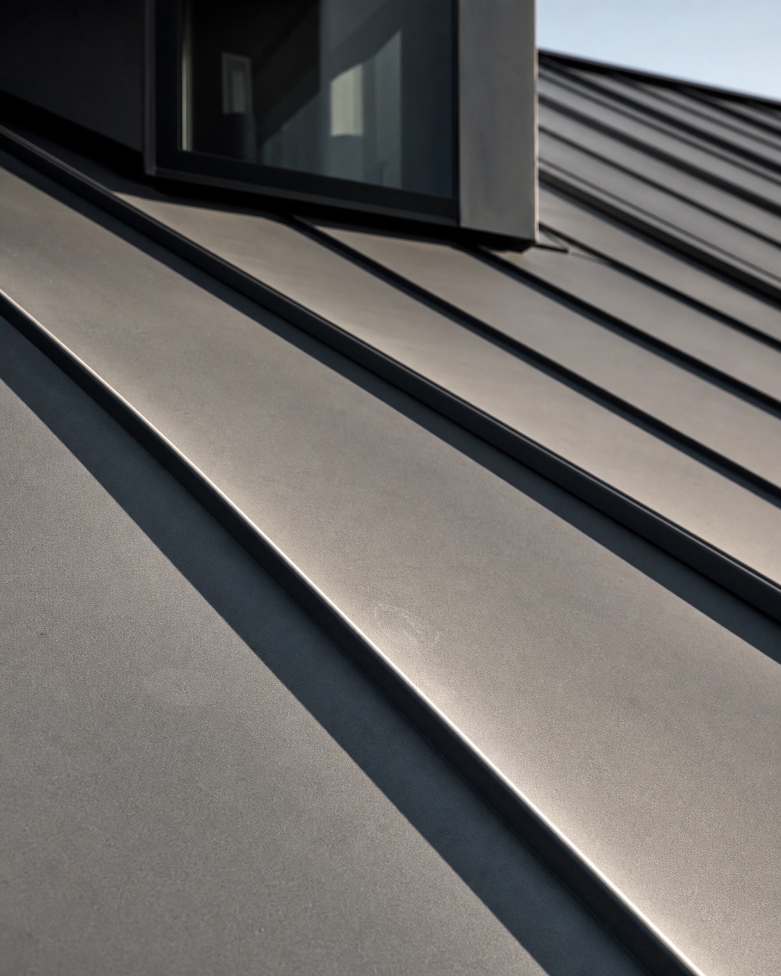 Close-up of matte gray standing-seam metal roof panels in late morning light