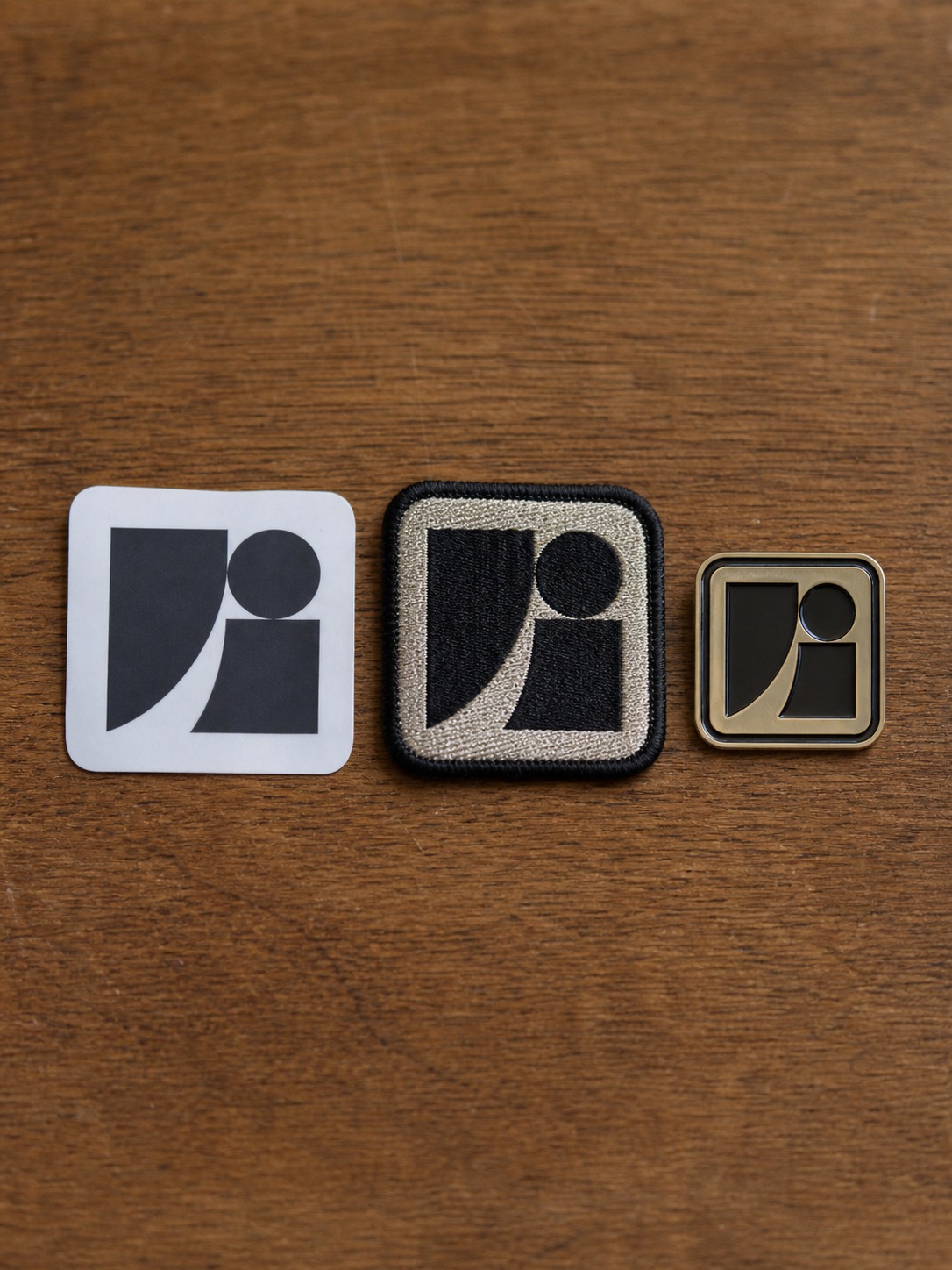 Sticker patch and pin comparison The same abstract brand mark adapted across a sticker, embroidered patch, and metal pin. | Sky Rye Design The same abstract brand mark adapted across a sticker, embroidered patch, and metal pin.