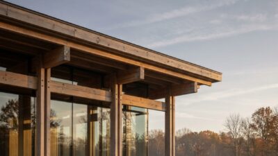 Modern timber-framed house with exposed glulam beams seen through a glass wall at golden hour.