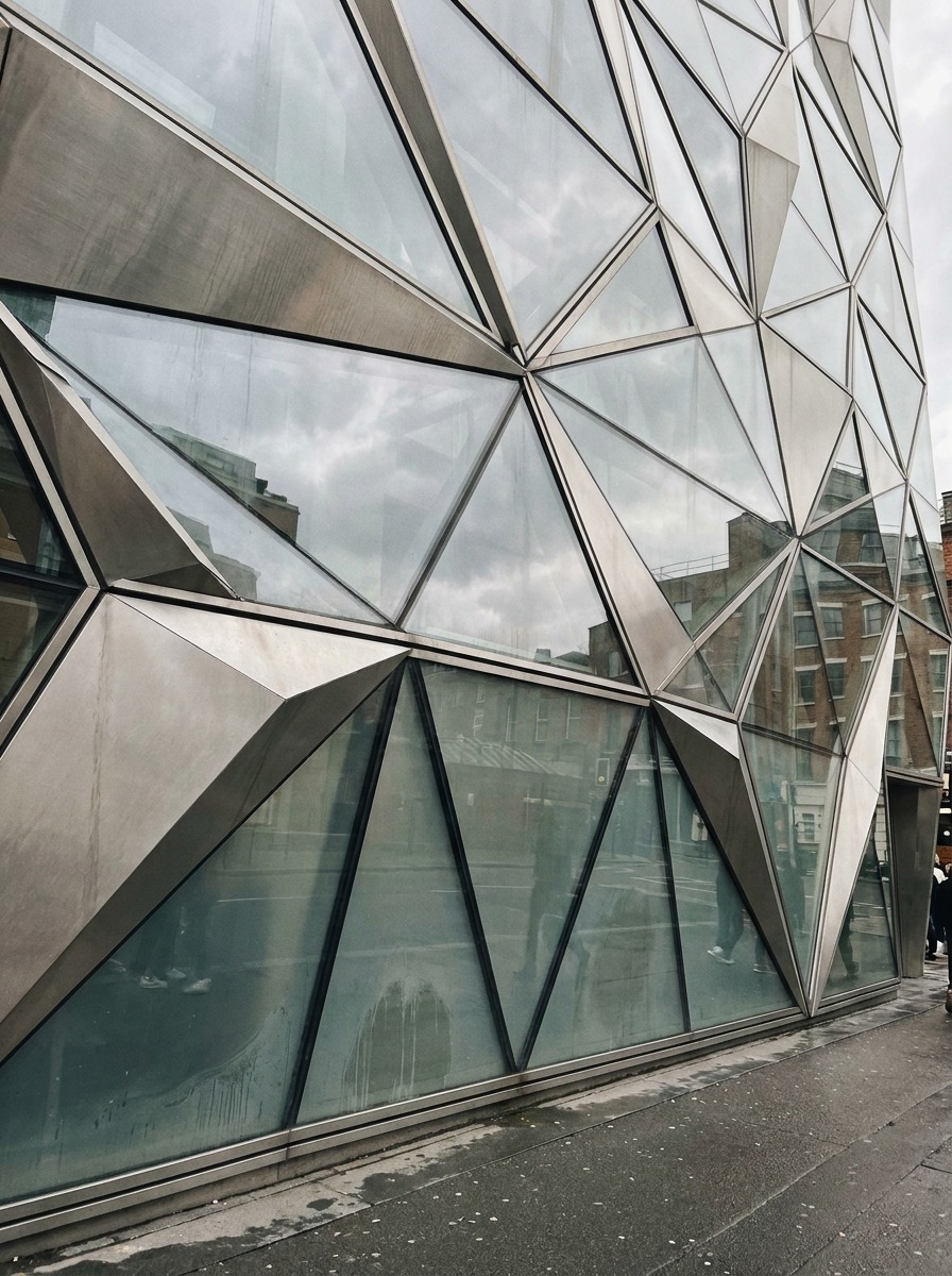 Modern glass and steel facade with a complex triangulated parametric panel pattern.